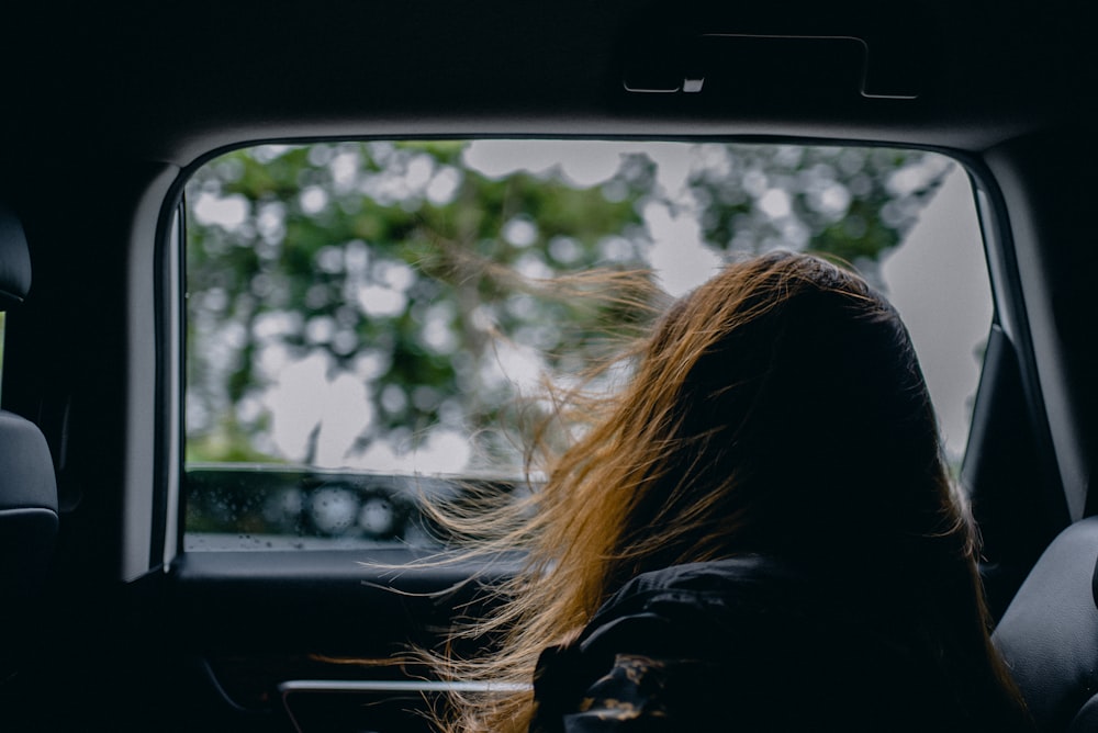 Mujer con chaqueta negra sentada dentro del coche durante el día