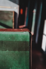A close-up of a worn, green fabric surface with a brown edge, possibly part of a seat or cushion, with a blurred background in a dimly lit setting.
