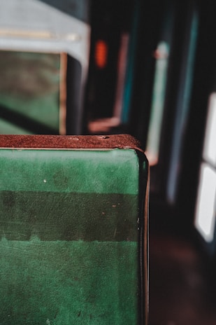 A close-up of a worn, green fabric surface with a brown edge, possibly part of a seat or cushion, with a blurred background in a dimly lit setting.