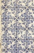 Blue and white ceramic tiles featuring ornate floral patterns with symmetrical designs. The tile arrangement is consistent and repeats across the surface, showcasing a traditional and decorative style.
