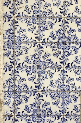 Blue and white ceramic tiles featuring ornate floral patterns with symmetrical designs. The tile arrangement is consistent and repeats across the surface, showcasing a traditional and decorative style.