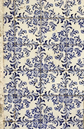Blue and white ceramic tiles featuring ornate floral patterns with symmetrical designs. The tile arrangement is consistent and repeats across the surface, showcasing a traditional and decorative style.