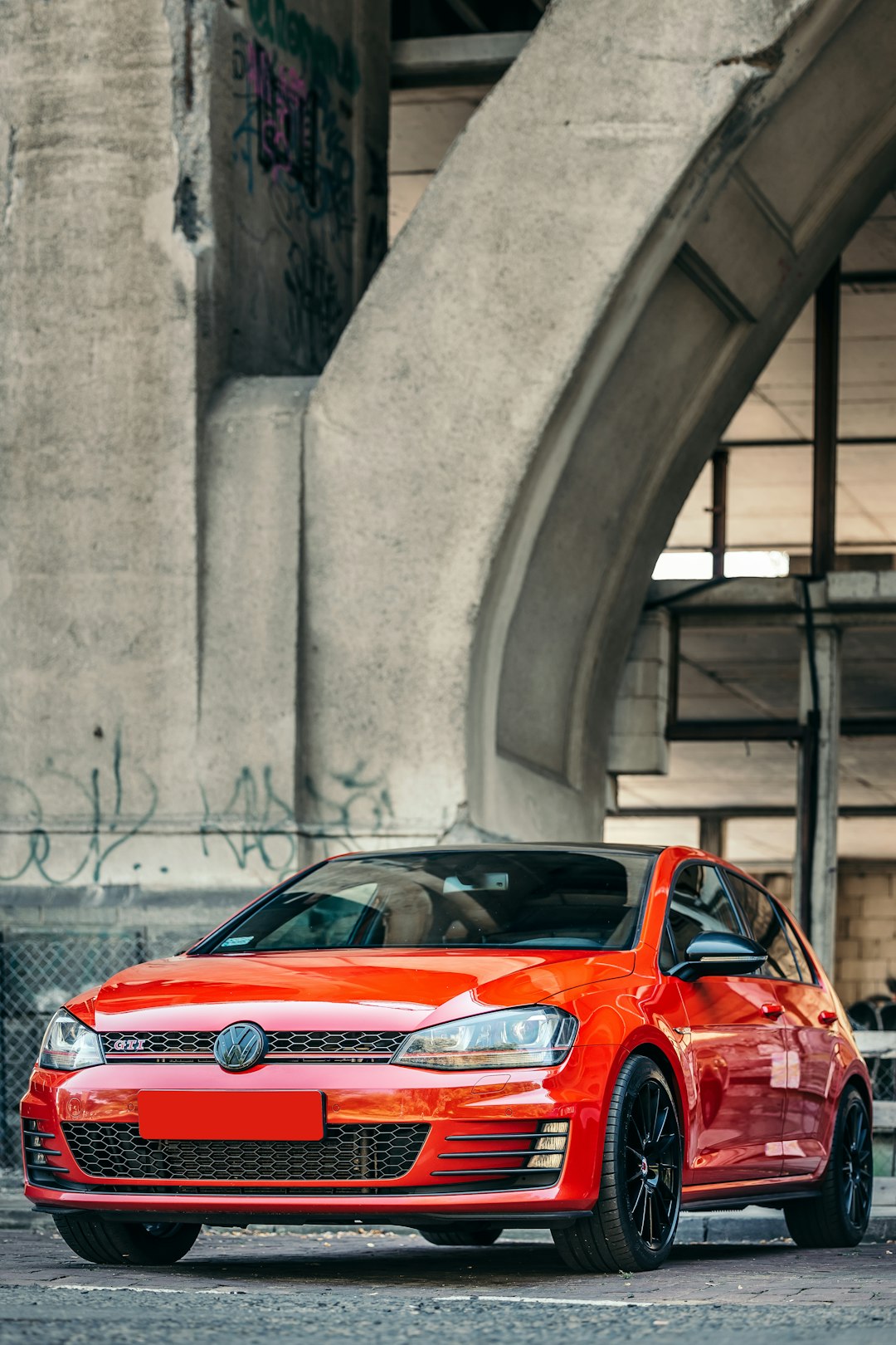 red car parked beside gray concrete wall