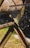 A close-up view of a saw cutting through a thick piece of wood, with sawdust particles scattering in the air. The rusty metallic saw is supported by a sturdy stand, and natural lighting enhances the texture of the wood and metal.