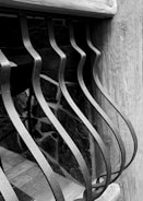 Curved metal bars form an artistic pattern against a wooden and stone background, creating a contrast between the smooth metal and the textured natural materials.
