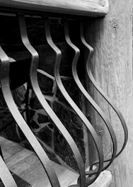 Curved metal bars form an artistic pattern against a wooden and stone background, creating a contrast between the smooth metal and the textured natural materials.