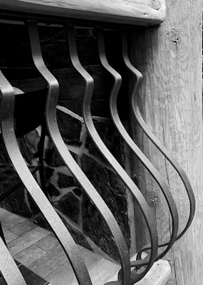 Curved metal bars form an artistic pattern against a wooden and stone background, creating a contrast between the smooth metal and the textured natural materials.