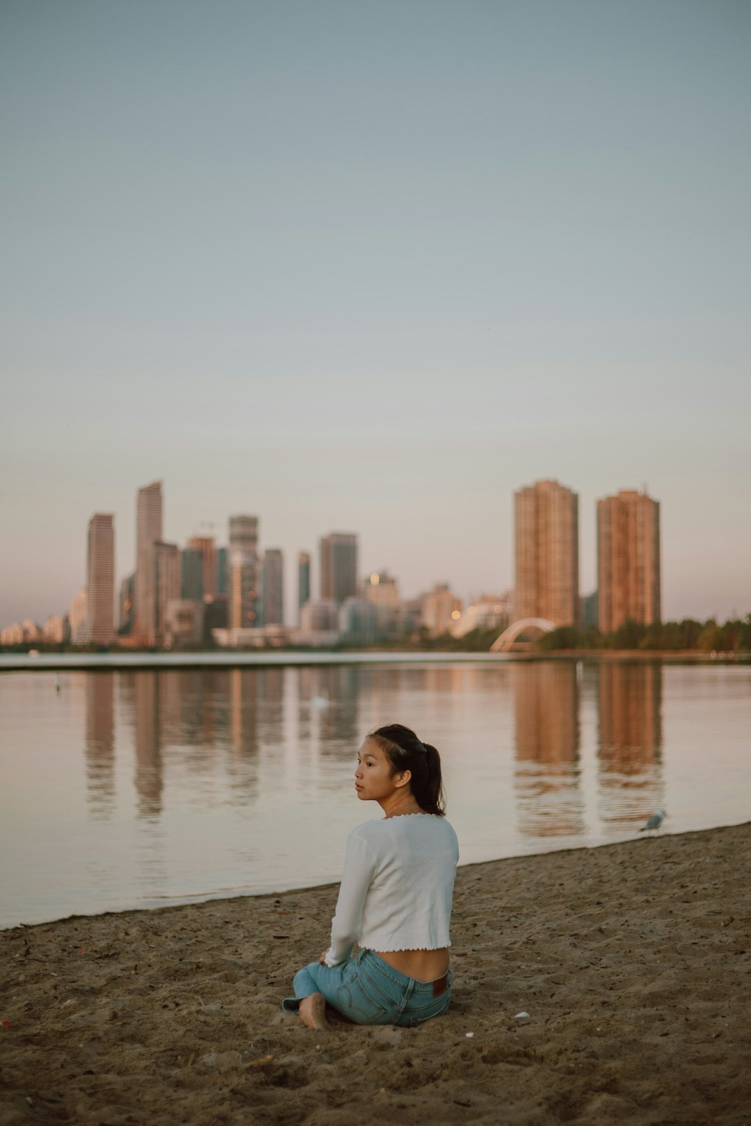 woman in white shirt sitting on brown sand near body of water during daytime