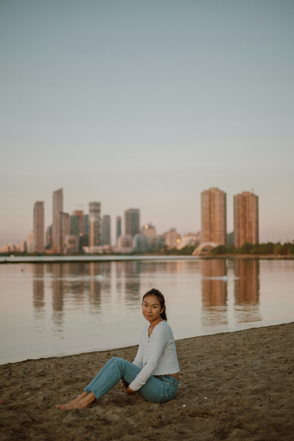 woman in white long sleeve shirt sitting on gray concrete bench near body of water during
