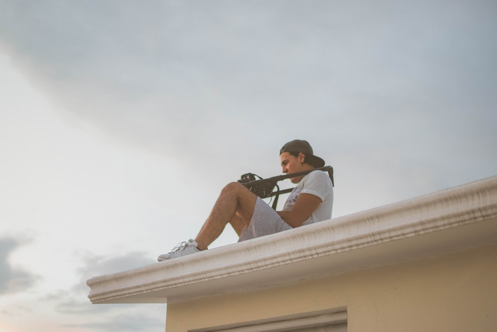 man in black t-shirt and blue denim shorts sitting on white concrete wall during daytime