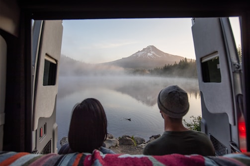 A misty early morning view of a camper van parked beside a serene Scottish loch with a golf course in the background.