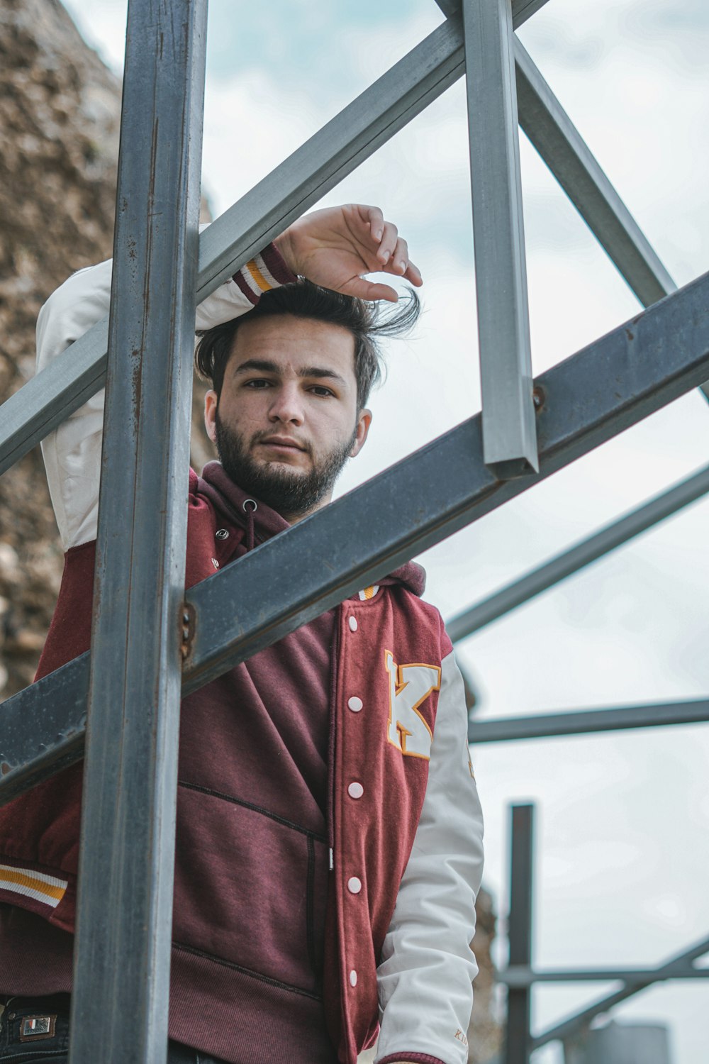 man in red jacket standing beside white metal frame during daytime