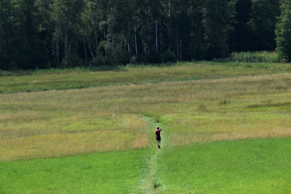 person in red shirt walking on green grass field during daytime