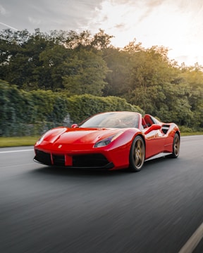 A sleek red convertible cruising along a coastal European road under a clear blue sky.