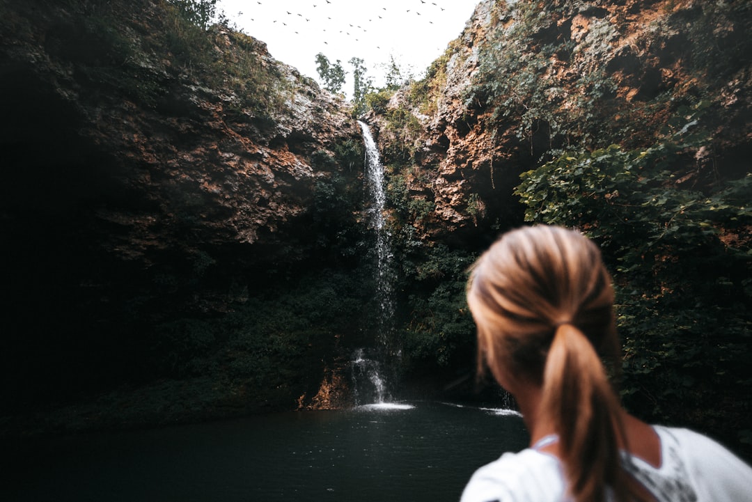 woman in white shirt standing in front of waterfalls during daytime