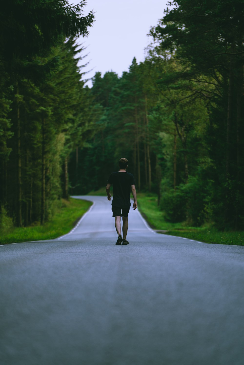 Hombre con camiseta negra y pantalones cortos negros caminando por la carretera durante el día
