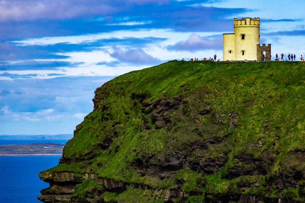 white concrete building on green mountain beside sea under blue sky during daytime