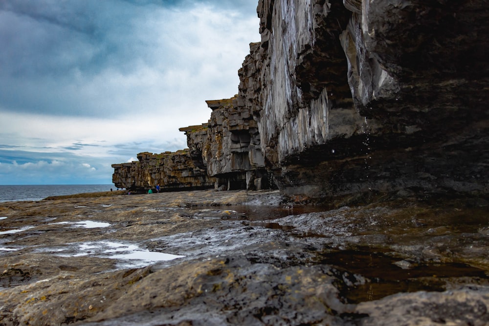 Grauer felsiger Berg am Meer unter weißen Wolken tagsüber