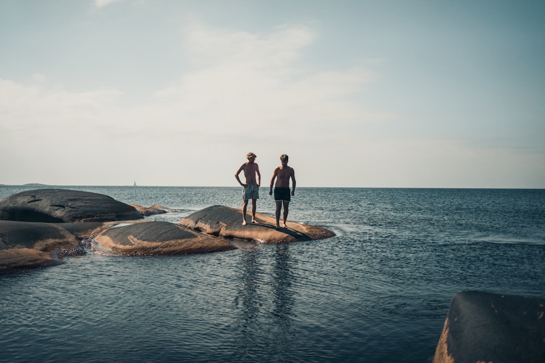 2 women standing on brown rock in the middle of sea during daytime