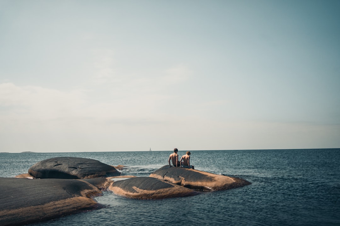 man and woman sitting on rock formation near sea during daytime