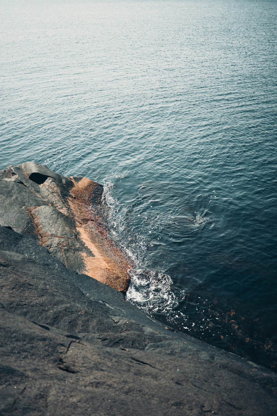 Rocky cliff overlooking ocean with splashed water creating contrast between solid rock and liquid water