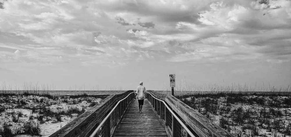 grayscale photo of man and woman walking on wooden bridge