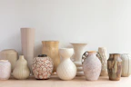 A collection of colorful stoneware vases arranged on a shelf with soft morning light.