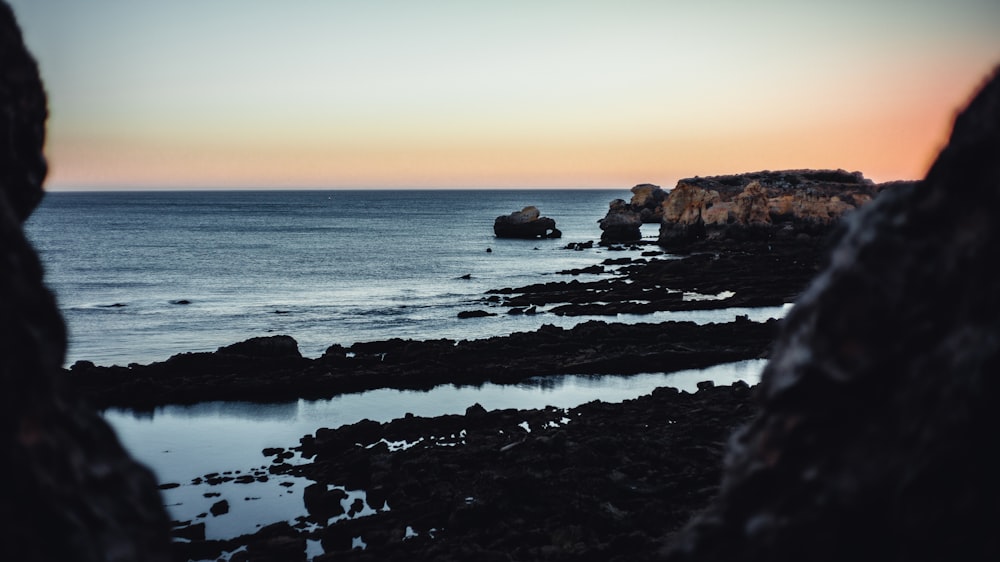 body of water near brown rock formation during sunset