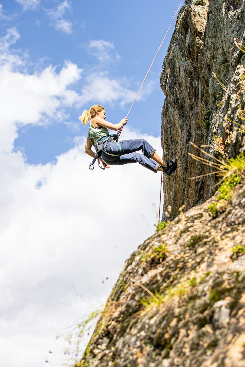 a woman climbing up a cliff on a rope