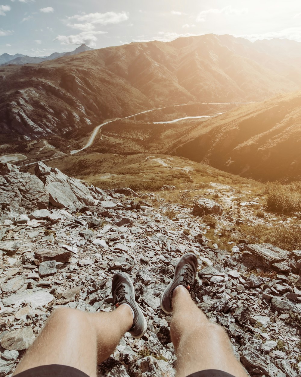 person in black and white sneakers sitting on rocky ground during daytime