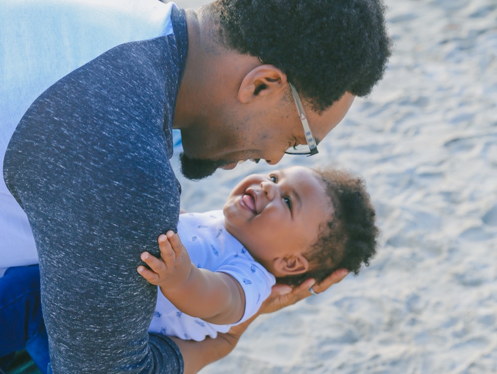 man in gray sweater carrying baby in white shirt