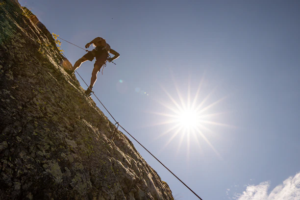 Instructor guiding a small group through rope handling on a sunlit rock face.