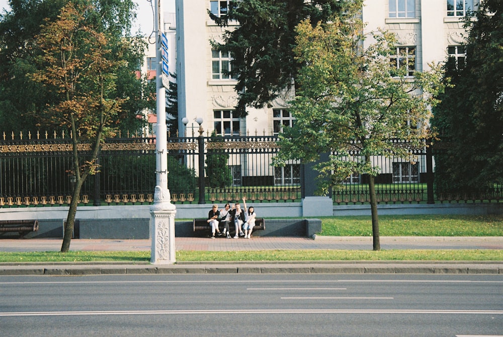people sitting on bench near green trees and white concrete building during daytime