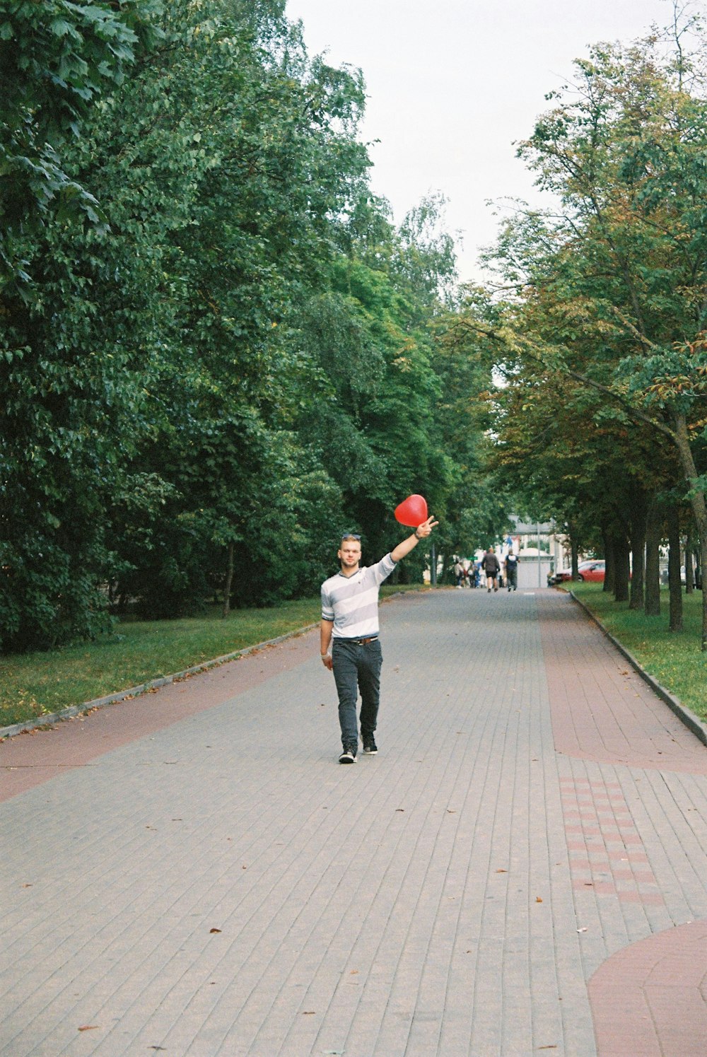 man in white shirt and black pants holding red ball walking on sidewalk during daytime