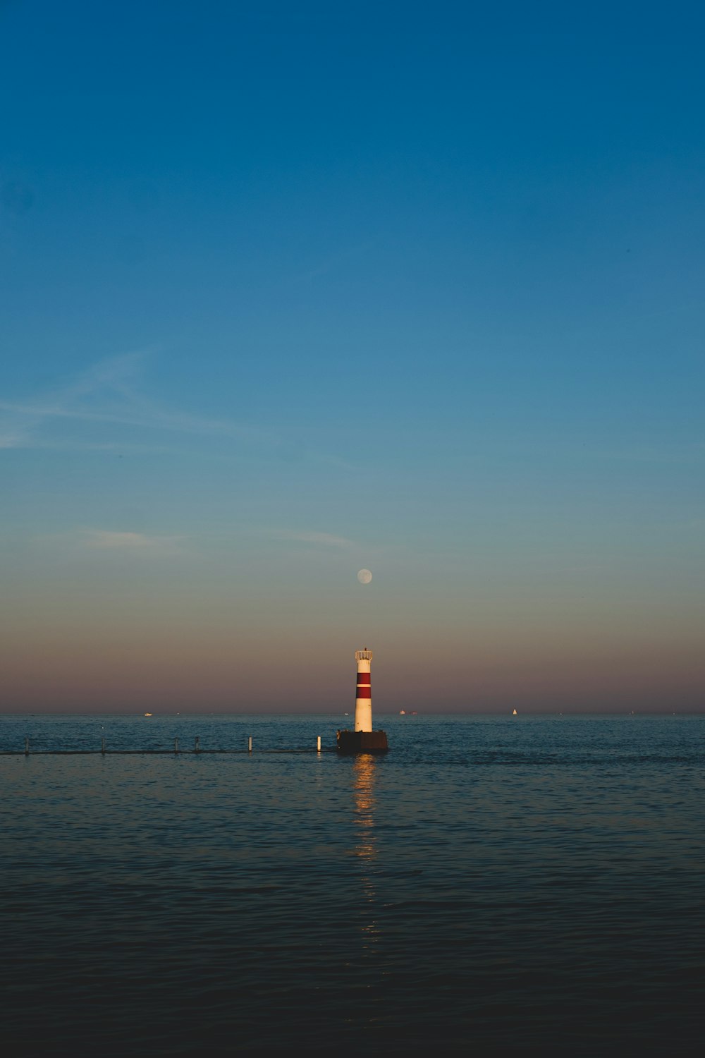 red and white lighthouse on sea under blue sky during daytime