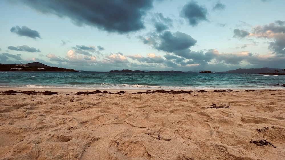 praia de areia marrom sob céu nublado durante o dia