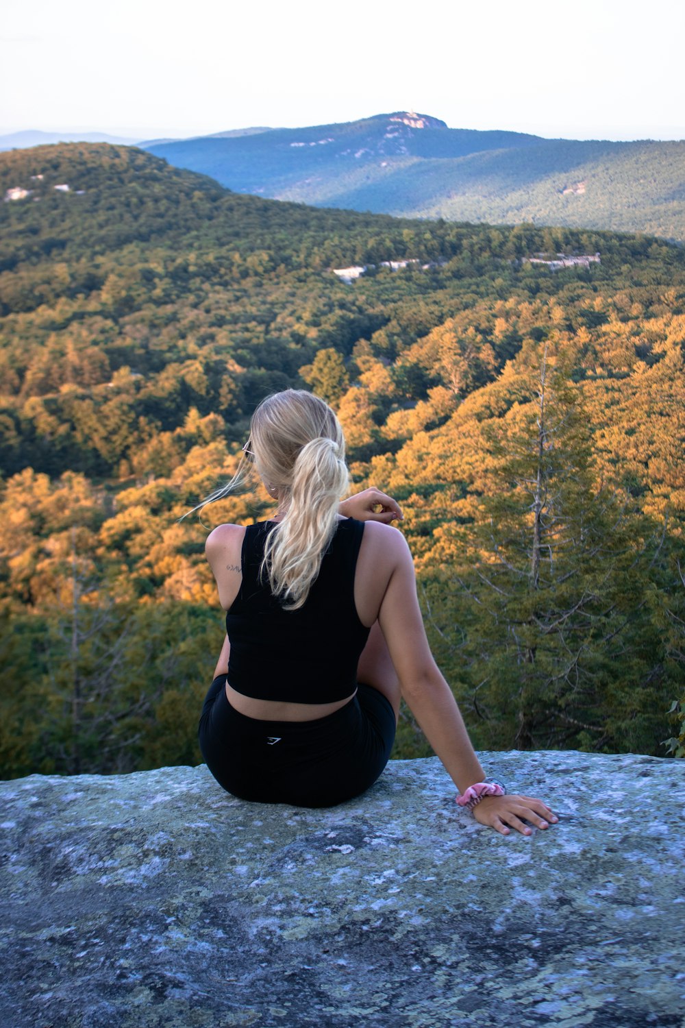 woman in black tank top sitting on rock near river during daytime