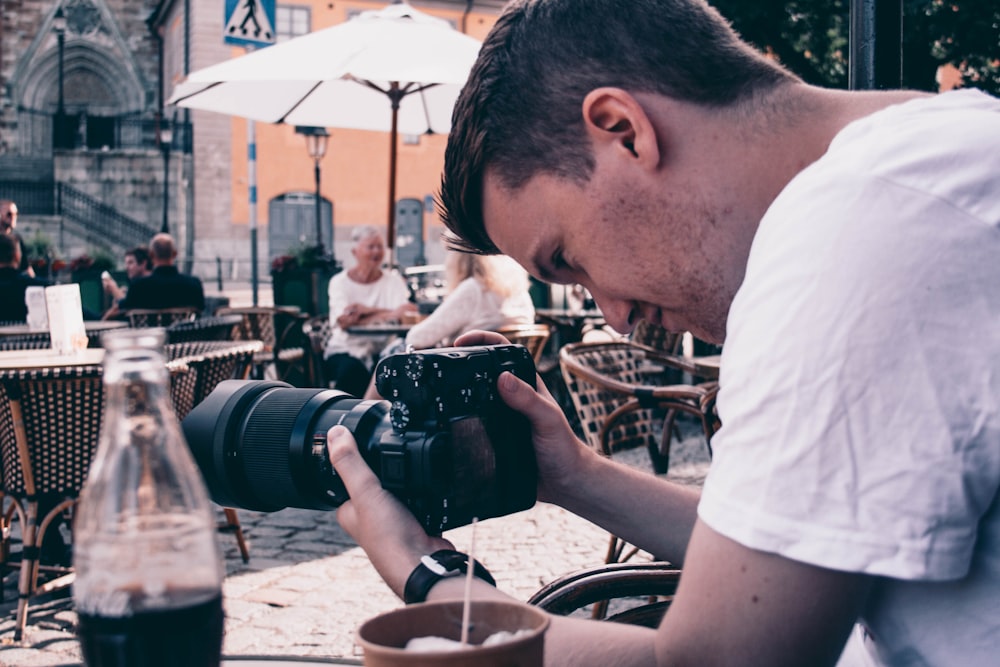 man in white shirt holding black dslr camera