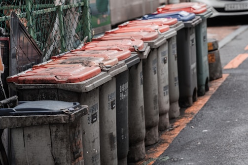 Metallic outdoor trash bins lined up in a public park setting.