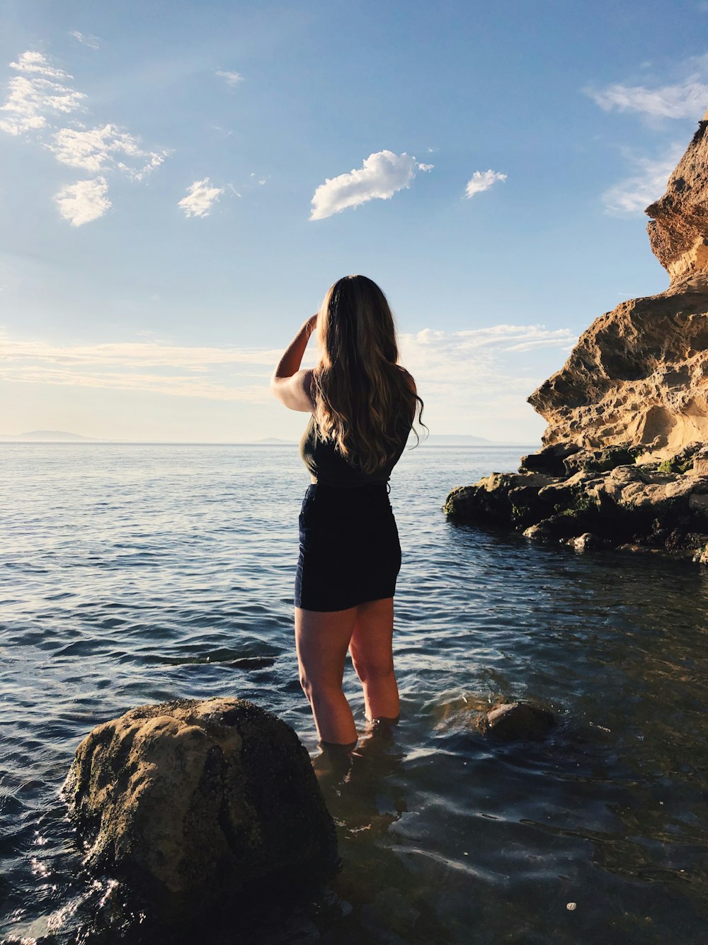 woman in black tank top and black shorts standing on rocky shore during daytime