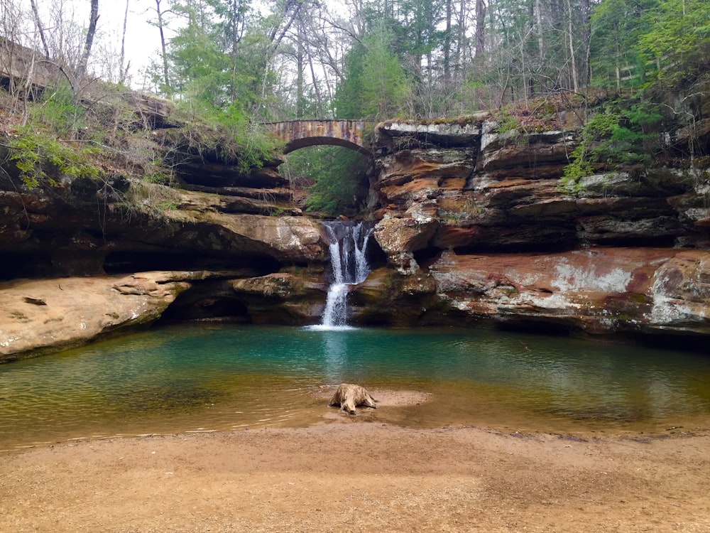 woman in white shirt sitting on brown rock near waterfalls during daytime