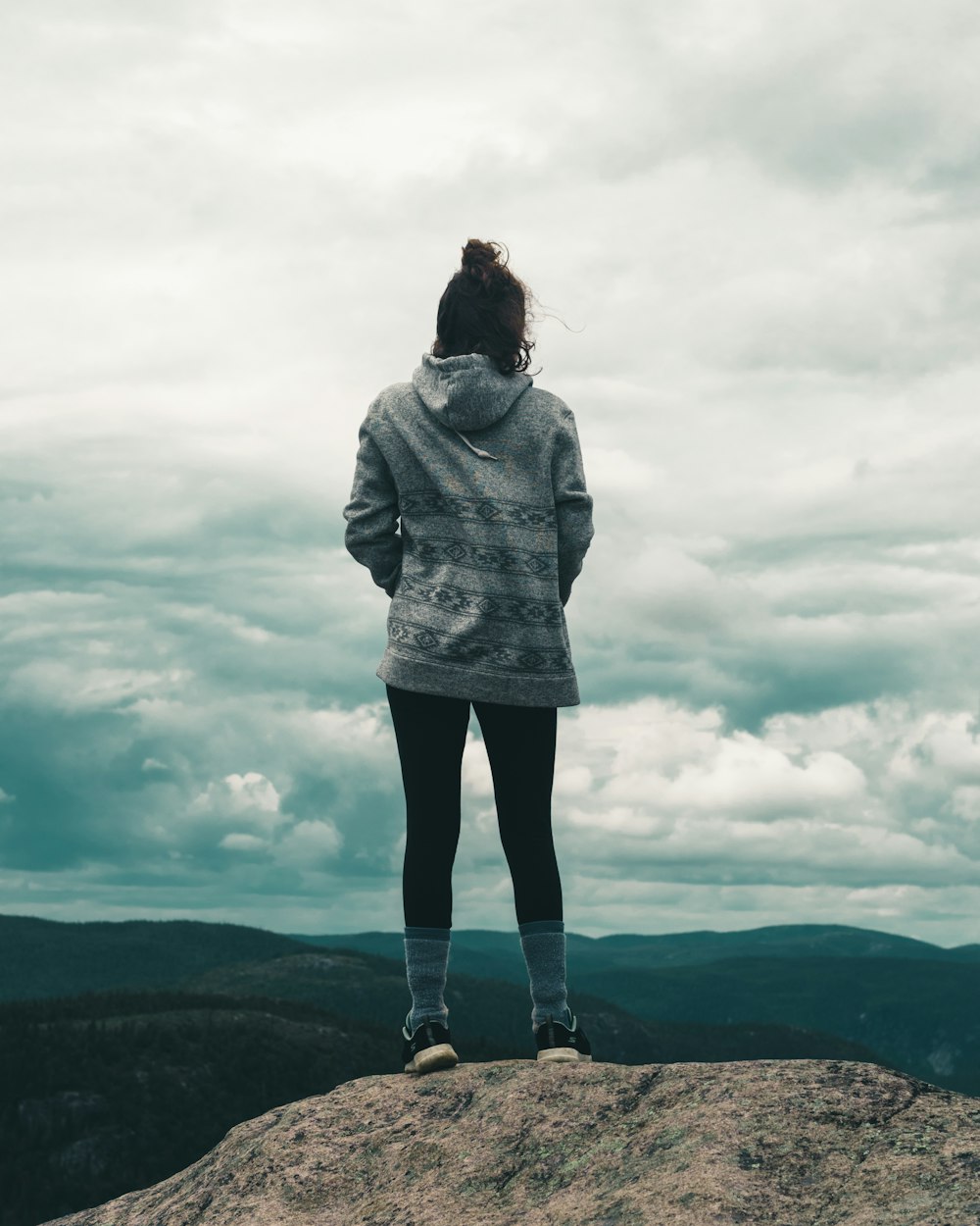 woman in gray hoodie standing on brown rock