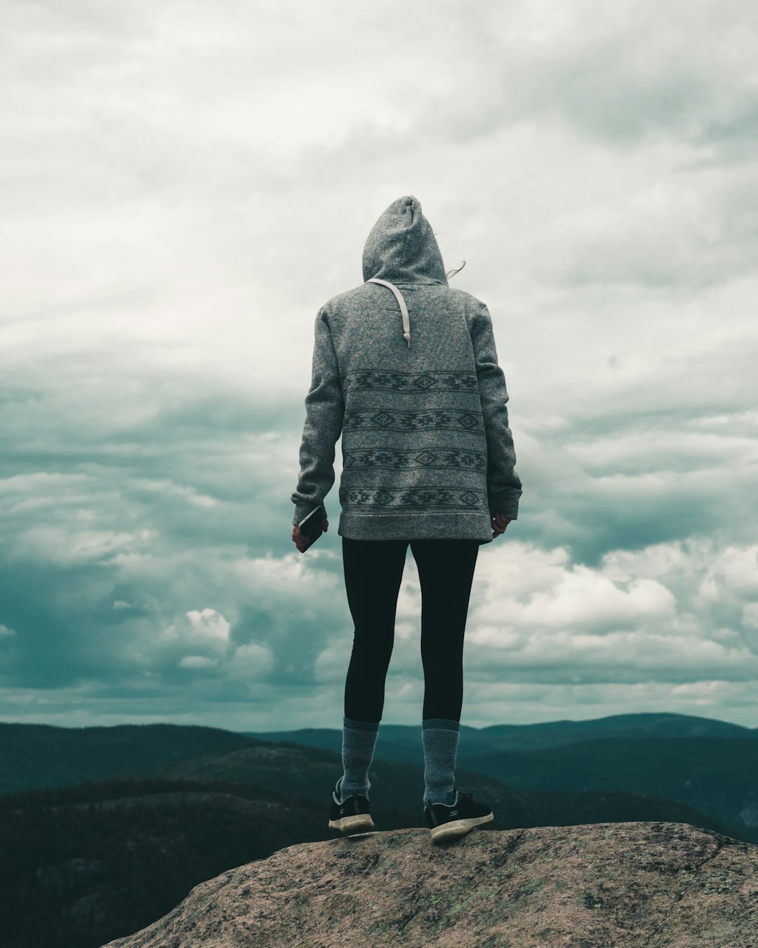 woman in gray hoodie standing on brown field under white clouds during daytime