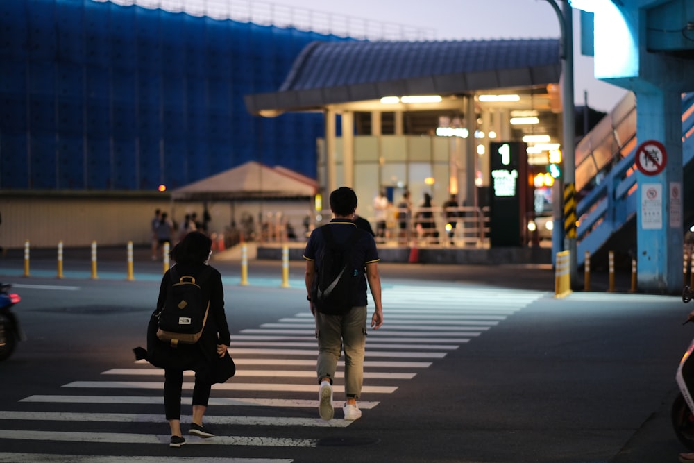 man in black jacket and white pants walking on sidewalk during night time