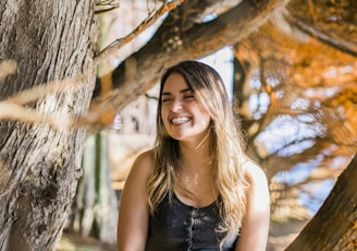 woman in black tank top sitting on tree trunk during daytime