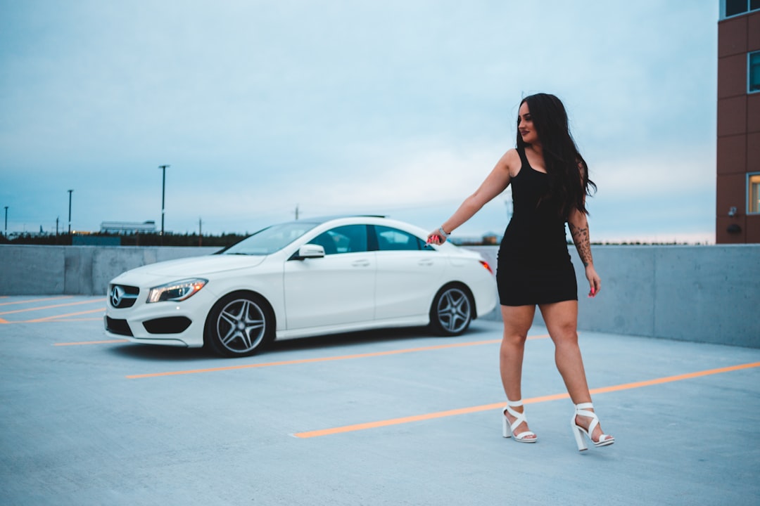 woman in black dress standing beside white coupe during daytime