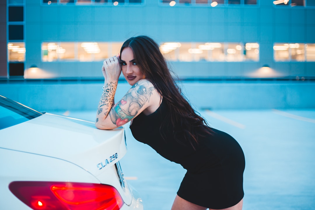 woman in black tank top and black shorts leaning on white car