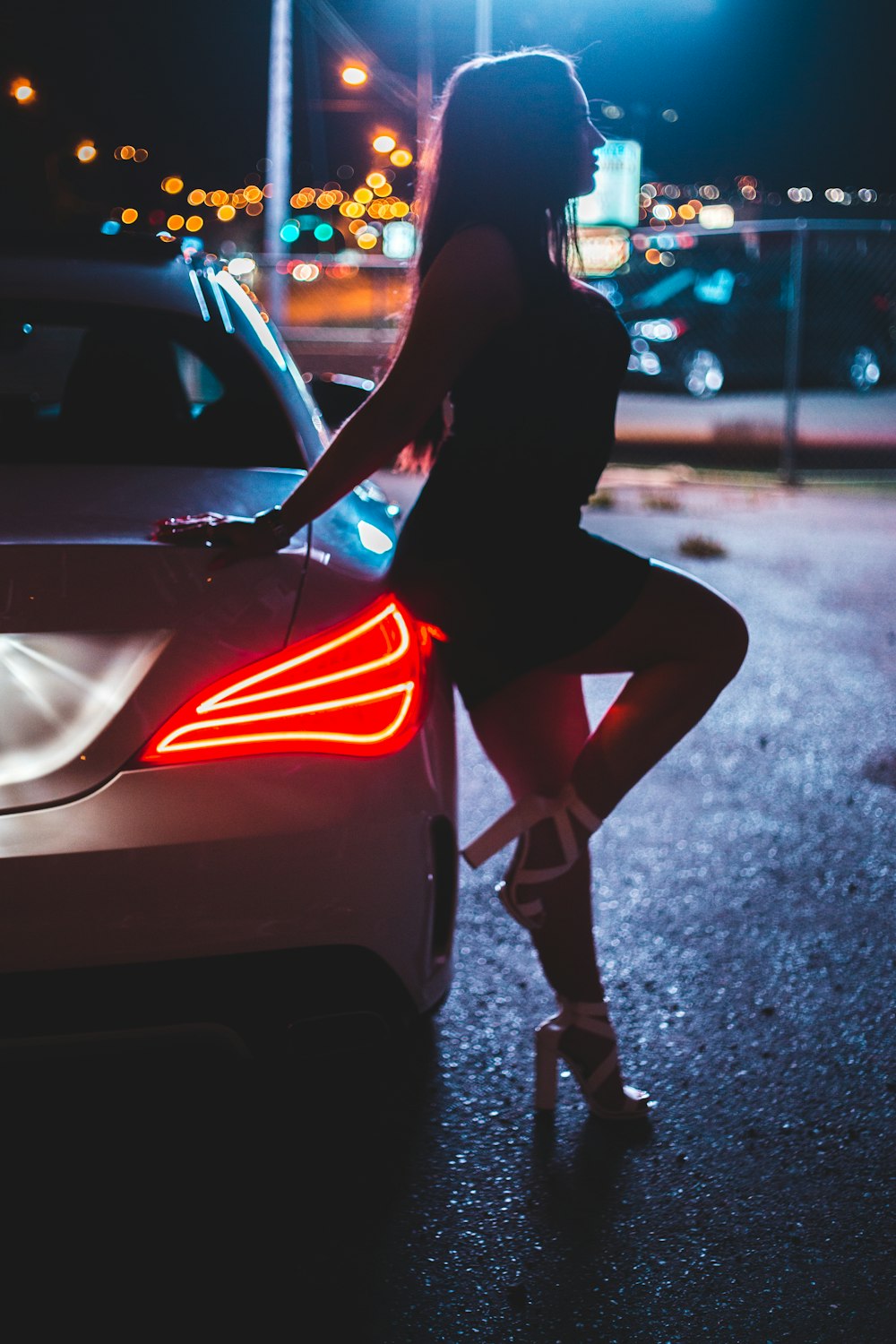 woman in black long sleeve shirt and red skirt standing beside black car during night time