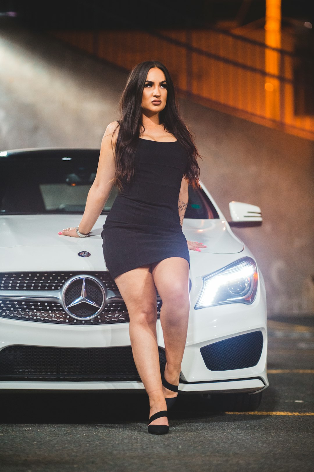 woman in black tank top and blue denim shorts standing beside white mercedes benz car