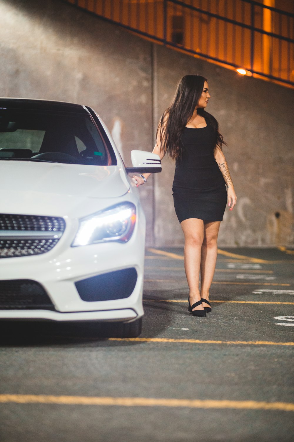 woman in black mini dress standing beside white car during daytime